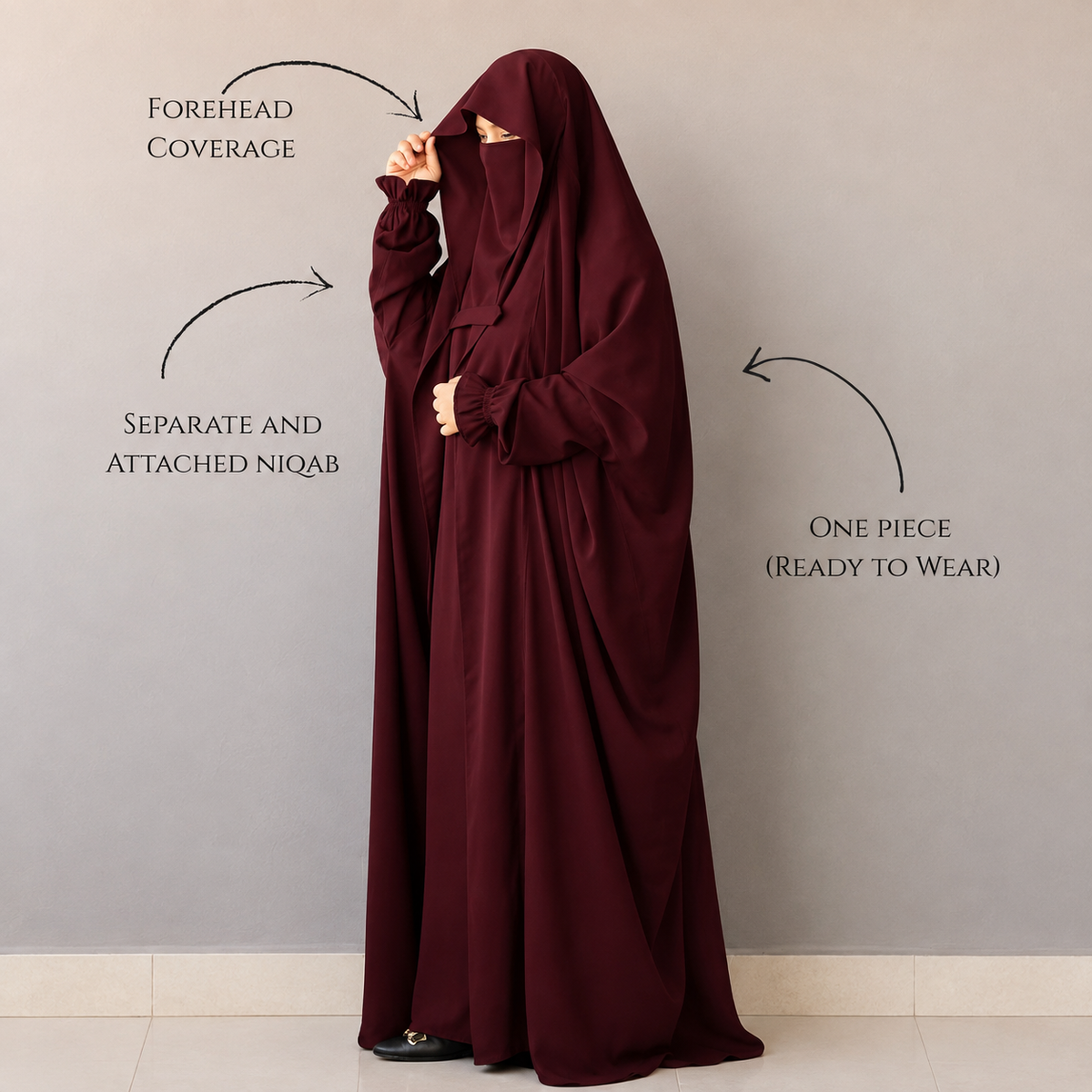 A woman wearing a deep burgundy abaya and matching niqab stands against a plain gray wall. Arrows and text call out features: forehead coverage, separate and attached niqab, and one-piece ready-to-wear design.
