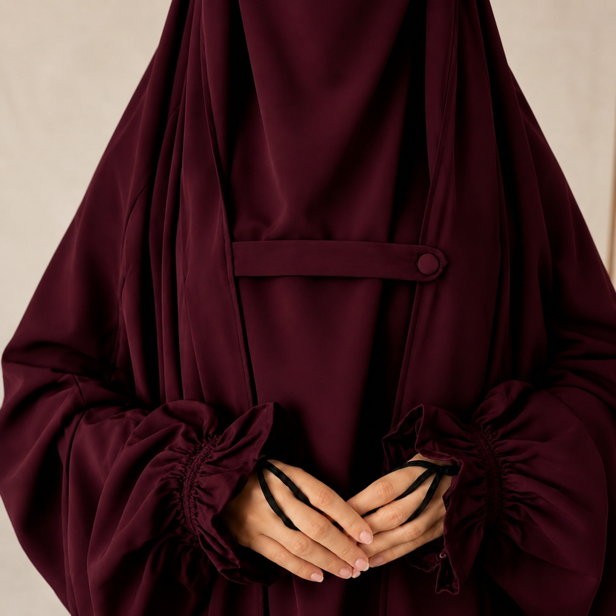 A close-up of a person wearing Womeo’s Maroon Saudi Jilbab or abaya with long gathered sleeves and a matching waist tie, shown against a soft beige background.